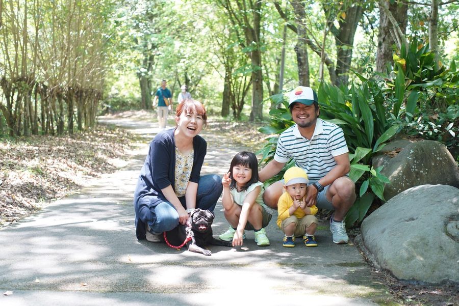 木漏れ日の道で犬と並ぶ家族